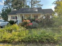 Charming home featuring solar panels, a cozy porch, and beautiful flowerbeds filled with colorful flowers and plants at 5404 Drum Inlet Pl, Raleigh, NC 27610