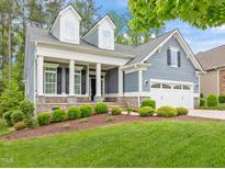 Charming blue home featuring a manicured lawn, stone accents, and a welcoming covered front porch at 1620 Hasentree Villa Ln, Wake Forest, NC 27587