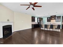 Open-concept living room featuring a fireplace, ceiling fan, and dark hardwood floors flowing into the modern kitchen at 2008 Campana Dr, Raleigh, NC 27603