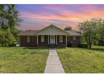 Charming brick home with a manicured lawn and inviting front porch under a beautiful sunset sky at 1303 Cherry Dr, Burlington, NC 27215