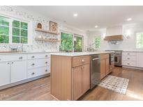 Bright kitchen with stainless steel appliances, light wood cabinets, an island and open shelving at 3009 Hillmer Dr, Raleigh, NC 27609