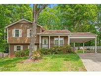 Split level home with brown siding, covered parking, and a charming front porch with flowering shrubbery at 300 Wakewood Ct, Raleigh, NC 27615