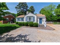 Charming single-story home featuring blue shutters, fresh landscaping, and gravel driveway on a sunny day at 713 E Whitaker Mill Rd, Raleigh, NC 27608