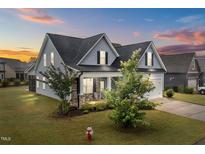 Charming two-story home featuring stone accents, a covered porch, and a manicured lawn at sunset at 47 Scarlet Bell Dr, Youngsville, NC 27596