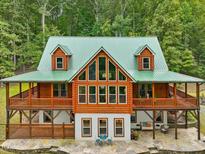 Stunning log home with green metal roof, large windows and wraparound porch surrounded by lush greenery at 123 Beech Forest Way, Pittsboro, NC 27312