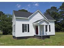 Charming white home with black shutters, front porch, and a well-manicured lawn and mature trees in the background at 305 E Harnett St, Benson, NC 27504