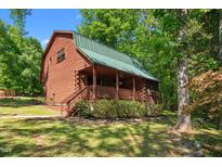 Charming log cabin home with a green metal roof and a welcoming front porch surrounded by lush greenery at 515 Tramway West Rd, Sanford, NC 27330
