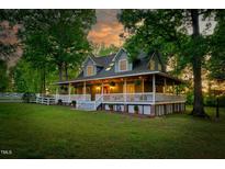 Charming home with a wraparound porch, white railings, lush lawn and mature trees create a serene setting at 54 Malcolm Neal Path, Louisburg, NC 27549
