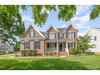 Charming brick two-story home featuring lush lawn and inviting front porch with white rails and blue shutters at 9251 Palm Bay Cir, Raleigh, NC 27617