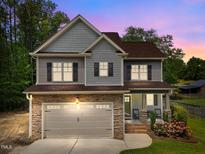 Charming two-story home with stone accents, gray siding, and a well-manicured lawn at twilight at 104 Anderson Park Dr, Wake Forest, NC 27596