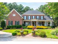 Stately brick home features a covered porch, lush landscaping, and manicured lawn at 1501 Samuel Wait Ln, Wake Forest, NC 27587