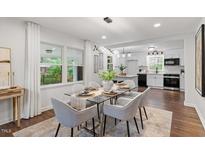 Bright dining room featuring a glass-top table, modern lighting, and a view to the adjacent kitchen with white cabinets at 3907 Inwood Dr, Durham, NC 27705