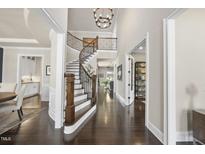 Elegant foyer with a curved staircase, dark wood floors, and a view into the kitchen and living spaces at 113 Amberwing Ct, Holly Springs, NC 27540
