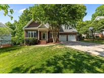 Charming brick home featuring a two-car garage, manicured lawn, and mature trees providing ample shade at 104 Crossway Ln, Holly Springs, NC 27540