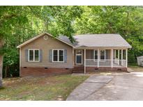Charming home with light brown siding, blue shutters, brick foundation and covered porch with white railings at 5600 Sherrif W Pl, Raleigh, NC 27610