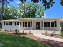 Charming brick ranch with white trim, blue shutters, a covered front porch, and mature landscaping at 5718 Woodcrest Dr, Raleigh, NC 27603