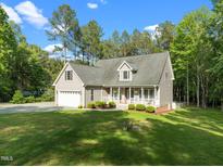 Charming home with a two-car garage, front porch, manicured lawn, and mature trees on a sunny day at 128 Madison Ct, Siler City, NC 27344