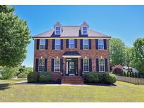 Charming two-story red brick home featuring black shutters, dormer windows, and well-maintained landscaping at 1009 Sarazen Dr, Clayton, NC 27527