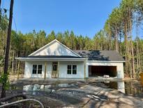 New construction home featuring white siding, a covered porch, and an attached garage, surrounded by a lush treeline at 214 Green Pines Estates Dr, Kenly, NC 27542