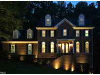 Striking two-story brick home featuring dormer windows, arched windows, and manicured landscaping illuminated at dusk at 5025 Martin Farm Rd, Raleigh, NC 27613