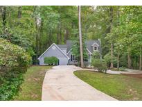 Charming gray home with a concrete driveway nestled in a lush, wooded landscape at 7116 Asheway Dr, Holly Springs, NC 27540