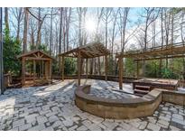 Beautiful outdoor patio featuring stone pavers, a hot tub, and wooden pergola structures in a wooded backyard at 7116 Asheway Dr, Holly Springs, NC 27540