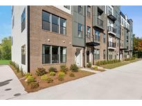 Modern townhome exterior featuring brick facade, black-framed windows, and landscaped front yard at 1242 Coach Station Aly # 101, Raleigh, NC 27601