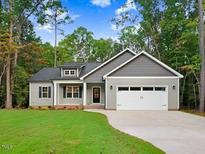 Charming single-story home featuring gray siding, a two-car garage, and a well-manicured front lawn surrounded by lush trees at 157 Gumtop Dr, Zebulon, NC 27597