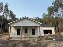 Charming single-story home with white siding, covered porch, and attached garage surrounded by natural landscaping at 240 Green Pines Estates Dr, Kenly, NC 27542