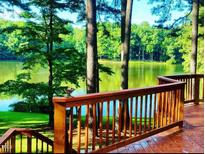 Inviting lake view from a wood deck featuring wooden rails and stairs surrounded by mature trees at 11813 Edgewater Ct, Raleigh, NC 27614