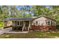 Charming single-story home with tan siding, brick foundation, and red shutters surrounded by mature trees at 702 Wedgewood Ave, Zebulon, NC 27597