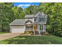 Charming two-story home with a yellow front door, lush landscaping, and a two car garage nestled amongst mature trees at 2513 Myrtle Ln, Hillsborough, NC 27278