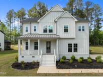 Charming two-story white home featuring a welcoming front porch, manicured lawn, and gray metal roof at 386 The Parks Dr, Pittsboro, NC 27312