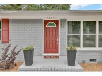 Charming home entrance with red door, brick facade, decorative planters, and ample natural light at 1007 Ancroft Ave, Durham, NC 27713