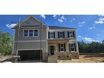 Two-story home with stone accents, black shutters, an open garage and covered front porch under a clear blue sky at 15 Guardian St, Youngsville, NC 27596