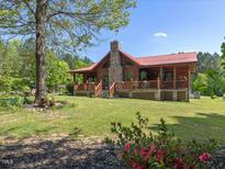 Inviting exterior showcasing a log cabin home with a stone chimney, front porch, and lush yard at 1656 Nc-42 Hwy, Moncure, NC 27559