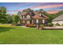 Stately home featuring stone accents, a manicured lawn, and a colorful sunset backdrop at 1508 Samuel Wait Ln, Wake Forest, NC 27587