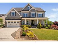 Beautiful two-story home with a stone and gray shingle exterior, lush landscaping, and a welcoming front porch at 7700 Stonehenge Farm Ln, Raleigh, NC 27613