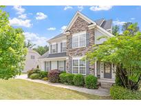 Charming two-story home featuring a stone facade, gray siding, manicured lawn, and lush landscaping at 113 Old Ballentine Way, Holly Springs, NC 27540