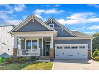 Charming home featuring a two-car garage, covered porch with stone accents and beautifully maintained lawn at 1665 Wilde Bnd, Apex, NC 27523