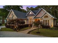 Inviting brick home with manicured lawn, landscape lighting and arched windows at sunset at 308 Thomas Dr, Clayton, NC 27520