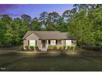 Charming single-story home featuring a cozy front porch, manicured landscaping, and a lush, wooded backdrop at 114 Cherryhill Dr, Four Oaks, NC 27524