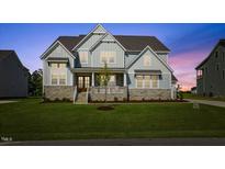 Charming two-story home featuring stone accents, gabled roof, and a well-manicured lawn at dusk at 8416 Brady Pointe Rd, Fuquay Varina, NC 27526