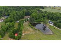 Expansive aerial view of estate featuring a large pond, fenced pastures, lush trees, and multiple outbuildings at 5237 Christian Light Rd, Fuquay Varina, NC 27526