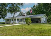 Ranch home with a covered porch, American flag, mature trees, and a circular driveway at 444 Barnette Rd, Louisburg, NC 27549