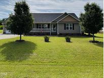 Charming single-story home featuring a covered porch and a well-manicured lawn with mature trees and landscaped features at 59 Long Grass Dr, Smithfield, NC 27577