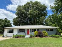 Charming single-story home featuring a manicured lawn, red front door, and lush landscaping at 704 S Mineral Springs Rd, Durham, NC 27703