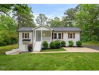 Charming brick home featuring a welcoming front porch, lush lawn, and beautifully landscaped shrubbery at 5020 Mimosa Dr, Durham, NC 27713