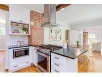 Modern kitchen with stainless steel appliances, white cabinetry, and brick accent wall over a hardwood floor at 800 E Forest Hills Blvd, Durham, NC 27707