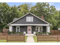 Charming one-story home featuring a pink front door and a cozy front porch, all surrounded by lush greenery and a lovely wood fence at 106 E Delafield Ave, Durham, NC 27704